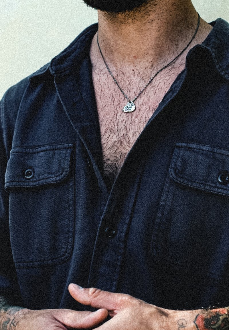 Svart skjorta med knappar, två framfickor, korta ärmar och ett silverhängsmycke. Strukturerad tyget och avslappnad passform.