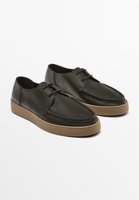 Chaussures décontractées en cuir noir à lacets avec design moc toe et semelles épaisses en caoutchouc marron clair, présentées côte à côte sur fond blanc.