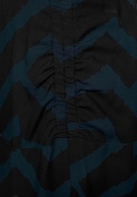 Černá tkanina s odvážným azurovým cik-cak vzorem. Má nabírané stehy podél středu, což vytváří texturované detaily.