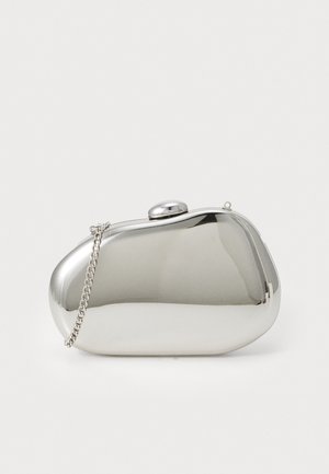 Kleine glänzende silberne Clutch mit geschwungenen Kanten und kurzem Kettenhenkel, die auf einer hellen Oberfläche liegt.
