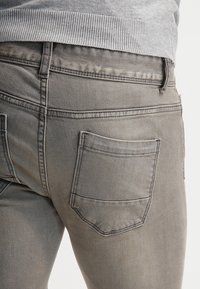 Jeans in denim grigio con una vestibilità slim, dotati di una tasca posteriore e una sottile texture sbiadita. La cintura è leggermente visibile sopra.