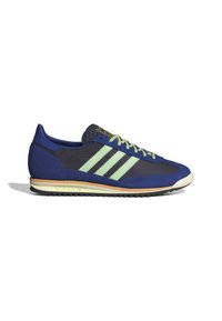Pantofii sport de culoare bleu marin cu un design verde cu trei dungi, material texturat la limbă, talpă de crem deschis și tread din cauciuc negru.