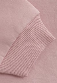 Rosa sweatshirttyg med en jämn textur och ribbade mudgester, som visar en konsistent färg och mjukhet genom hela plagget.