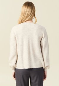 Ljusbeige stickad tröja med sänkta axlar, ribbad textur och cropped fåll. Mjuk material med subtila färgvariationer.