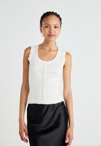 Débardeur blanc à côtes avec des bords festonnés et des détails de boutons, associé à une jupe noire en satin élégante. Texture lisse, design ajusté.