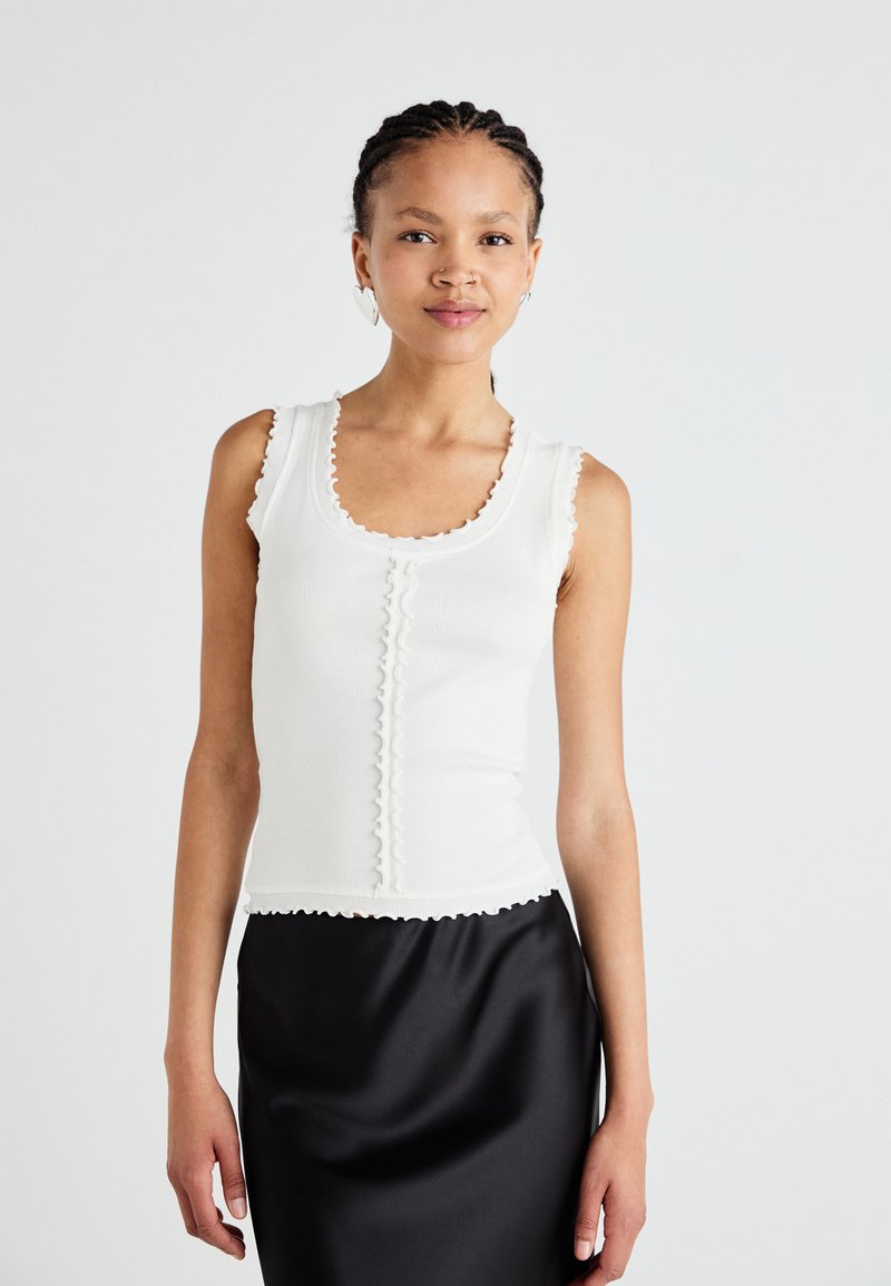 Débardeur blanc à côtes avec des bords festonnés et des détails de boutons, associé à une jupe noire en satin élégante. Texture lisse, design ajusté.