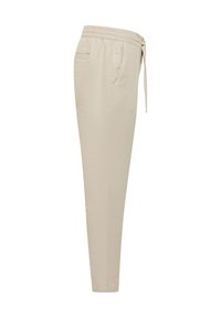 Pantalon beige fuselé avec taille élastique et cordon, poches latérales et poche passepoilée à l’arrière, vu de côté.
