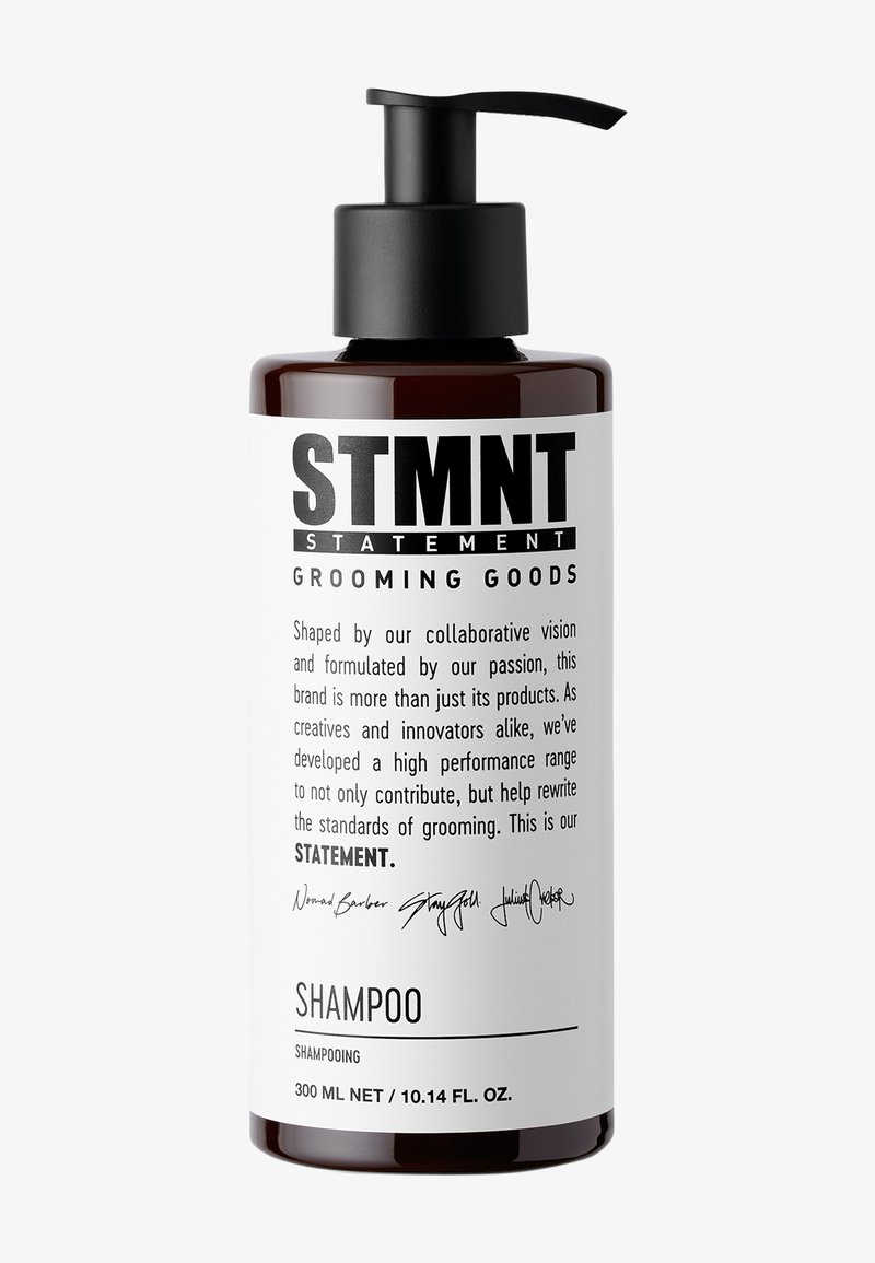 Braune Flasche mit schwarzem Pumpdeckel. Weißes Etikett mit schwarzem Text, auf dem "STMNT GROOMING GOODS" und "SHAMPOO" steht, darunter Volumenangaben.