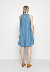 Dżinsowa sukienka w kształcie litery A bez rękawów, z detalem w postaci dziurki na plecach i miękką teksturą, zestawiona z beżowymi, teksturowanymi butami na obcasie.