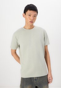 Ανοιχτό πράσινο κοντομάνικο T-shirt με υφή, στρογγυλή λαιμόκοψη και χαλαρή εφαρμογή. Συνδυασμένο με τζιν σορτς με φθαρμένη όψη.