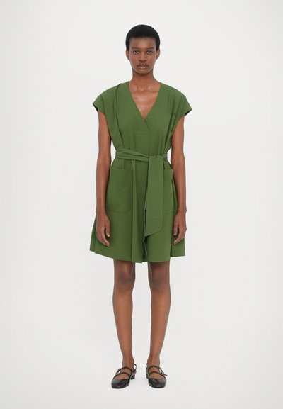 Robe portefeuille verte courte avec des manches courtes, un décolleté en V, une ceinture à nouer et deux poches avant. Texture lisse, design jusqu'au genou.