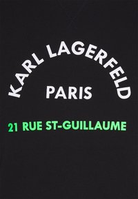Tissu noir avec texte blanc "KARL LAGERFELD PARIS" en arc et texte vert "21 RUE ST-GUILLAUME" en dessous.