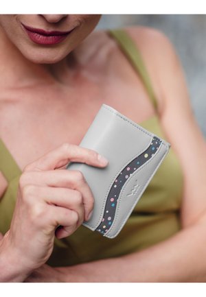 Světle šedá kožená peněženka s křivkovým designem, zdobená tmavě šedým akcentem a vícero barevnými tečkami. Hladký povrch, kompaktní tvar.