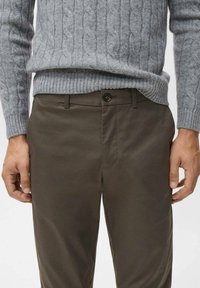 Suéter gris de punto trenzado con ribete acanalado, combinado con pantalones oscuros de color marrón que tienen un cierre de botón y un diseño de frente plano.