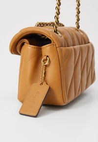 Brown quilted leather handbag with a rolled top, gold chain strap, zipper detail, and a leather tag attached. Matte finish, structured shape.