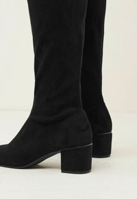 Bottes hautes jusqu'au genou en daim noir avec un bout carré et un talon bloc. Le design présente une texture lisse et un style minimaliste sans ornements.