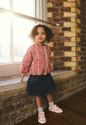 Red gingham checked jacket with white accents and buttons, paired with a dark denim skirt and pink sneakers with red dots. Curly hair.