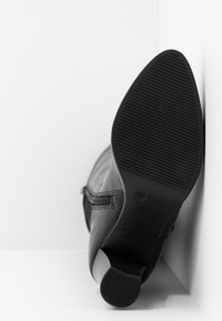 Bottine en cuir noir avec une finition lisse, semelle texturée, bout rond et fermeture à glissière sur le côté. Talon en caoutchouc et design de semelle à nervures.