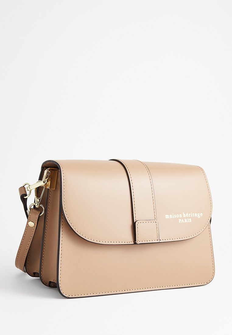 Beżowa skórzana torebka na ramię z klapką, regulowanym paskiem, złotymi akcentami oraz napisem "maison héritage PARIS" z przodu.