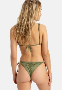 Žalias bikinis, turintis nugarėlėje rišamą viršų su plonomis petnešėlėmis ir raukšlėtu žemu apatiniu, pagamintas iš lygaus audinio su minimaliu tekstūros efektu.