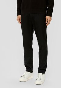 Zwarte taps toelopende broek van een gladde stof, met een platte voorkant, zijzakken en een standaard taille, gecombineerd met witte sneakers.