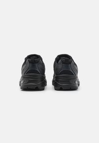 Chaussures de sport noires avec une tige en mesh et une semelle en caoutchouc, présentant des accents texturés, un talon arrondi et une languette à l'arrière pour un enfilage facile.