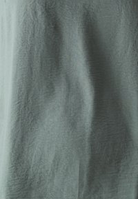 Texturerad tyg i dämpad grön, med lätta veck och en slät yta. Lätt och faller mjukt. Inga synliga mönster eller detaljer.