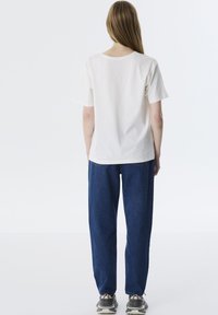 Weißes Kurzarm-T-Shirt mit Rundhalsausschnitt, kombiniert mit lockeren blauen Jeans. Das Outfit zeichnet sich durch eine lässige Passform und einen weichen Stoff aus.