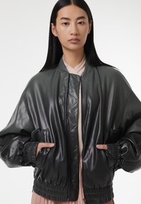 Veste bomber vert foncé en cuir brillant, avec un ourlet côtelé, une fermeture éclair et deux poches latérales.