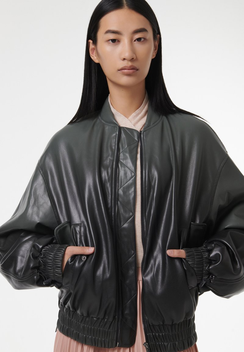 Veste bomber vert foncé en cuir brillant, avec un ourlet côtelé, une fermeture éclair et deux poches latérales.