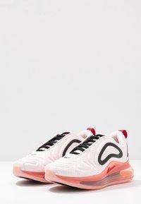 Buty sportowe z białym wierzchem, czarnymi sznurówkami, czerwonymi akcentami i przezroczystą różową podeszwą. Teksturowany wzór z gładkim wykończeniem.