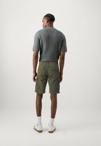 Polo shirt grigio a maniche corte in maglia con motivo testurizzato, abbinato a pantaloni cargo olive e sneakers bianche con suole color nocciola.