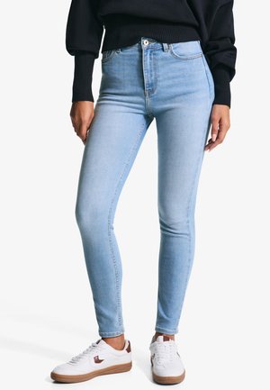 Jean skinny bleu clair en denim, avec une taille haute, un design à cinq poches et une texture lisse, associés à des baskets blanches.