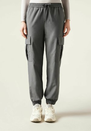 Grå cargobyxor med elastisk midja, sidofickor och elastiska benslut, tillsammans med beige sneakers. Slät textur.