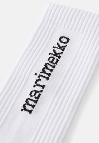 Bílé žebrované ponožky s černým logem Marimekko, s texturovaným povrchem a výrazným pleteným vzorem po celém povrchu.