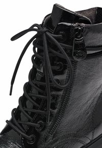 Black patent leather ankle boot with round toe, featuring lace-up design, side zipper, and textured surface.
