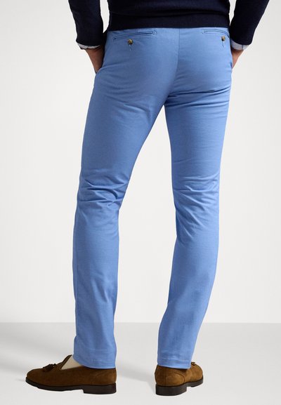 Ανοιχτό μπλε παντελόνια slim-fit με δύο πίσω τσέπες, κουμπιά και λεία υφή, συνδυασμένα με καφέ σουέτ μοκασίνια.