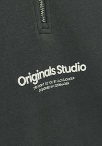 Sudadera gris oscuro con diseño de media cremallera, con la marca en texto blanco "Originals Studio" y detalles adicionales que indican la marca y el lugar de diseño.
