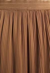 Jupe plissée d'une teinte marron chaud, dotée d'une ceinture texturée et d'un tissu fluide avec des plis verticaux, créant un effet doux et drapé.