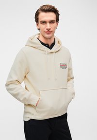 Φούτερ με κουκούλα σε κρεμ απόχρωση με μπροστινή τσέπη, κορδόνια και κεντημένο λογότυπο "TOMMY HILFIGER EST. 1985". Απαλό ύφασμα, άνετος σχεδιασμός.