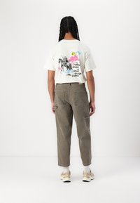 T-shirt graphique crème avec un imprimé coloré au dos, associé à un pantalon cargo vert olive avec de grandes poches et une coupe décontractée.