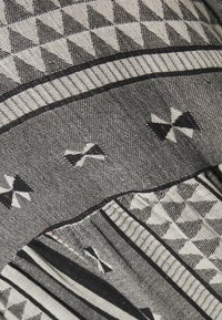 Gewebter Stoff in Schwarz und Weiß mit geometrischen Mustern, einschließlich Dreiecken und Streifen, mit einer strukturierten Oberfläche und kontrastierenden Akzenten.