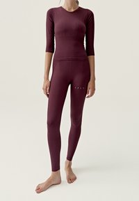 Burgundy träningsset som inkluderar en figurnära kortärmad topp med texturerad detalj och högmidjade leggings med små utskärningar.