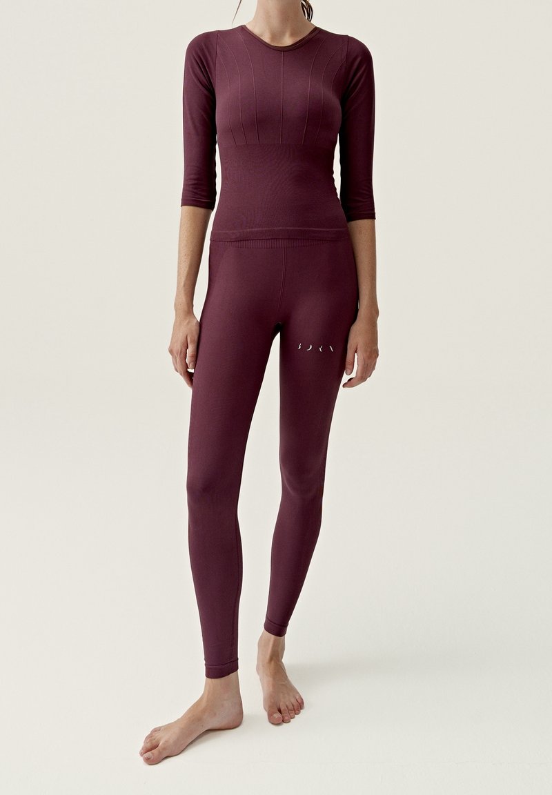 Burgundy träningsset som inkluderar en figurnära kortärmad topp med texturerad detalj och högmidjade leggings med små utskärningar.