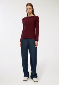 Burgundowy sweter z dzianiny z okrągłym dekoltem, zestawiony z luźnymi niebieskimi dżinsami i białymi trampkami. Gładka tekstura i luźny krój.