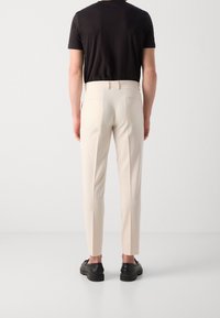 Beige skräddarsydda byxor med smal passform, som har en jämn textur och bakfickor, i kombination med en svart tajt t-shirt och svarta skor.