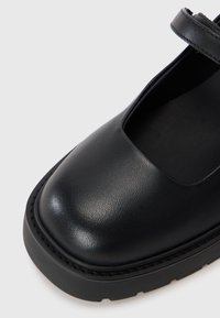 Scarpa in pelle nera con punta arrotondata, finitura testurizzata e una fascia larga sulla parte superiore. Presenta una suola spessa e robusta.