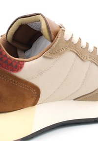 Sneaker in tessuto beige con dettagli in camoscio marrone, lacci bianchi e un tallone marrone texturizzato. Suola intermedia crema e suola esterna in gomma nera.