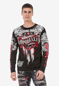 Schwarzes Langarm-T-Shirt mit grafischen Drucken in Rot und Weiß, darunter Sterne und Tiermotive, aus einem Baumwollmischgewebe gefertigt.