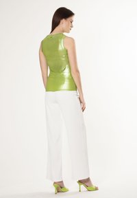 Groene, glanzende mouwloze top gecombineerd met lange witte broek en groene hoge hakken sandalen. De top heeft een aangesloten pasvorm en een gladde textuur.